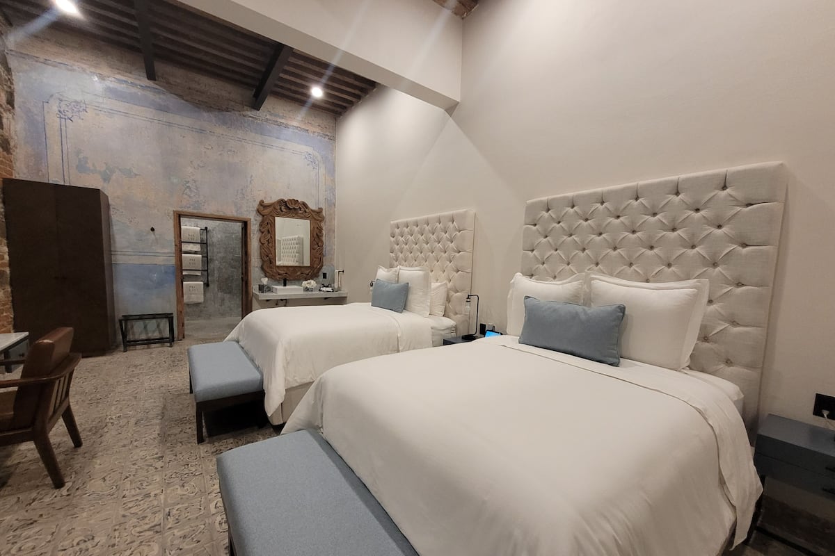A hotel room with two beds, a large mirror, a wooden door, and a small table.