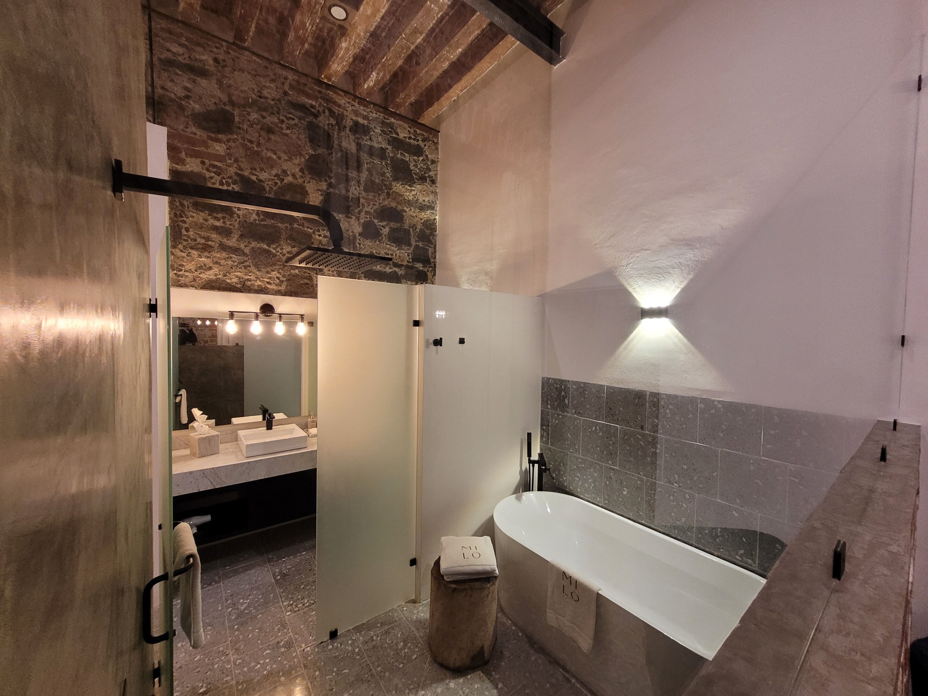 A modern bathroom with a stone wall, a large bathtub, and a vanity with a mirror.