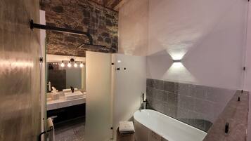 A modern bathroom with a stone wall, a large bathtub, and a vanity with a mirror.