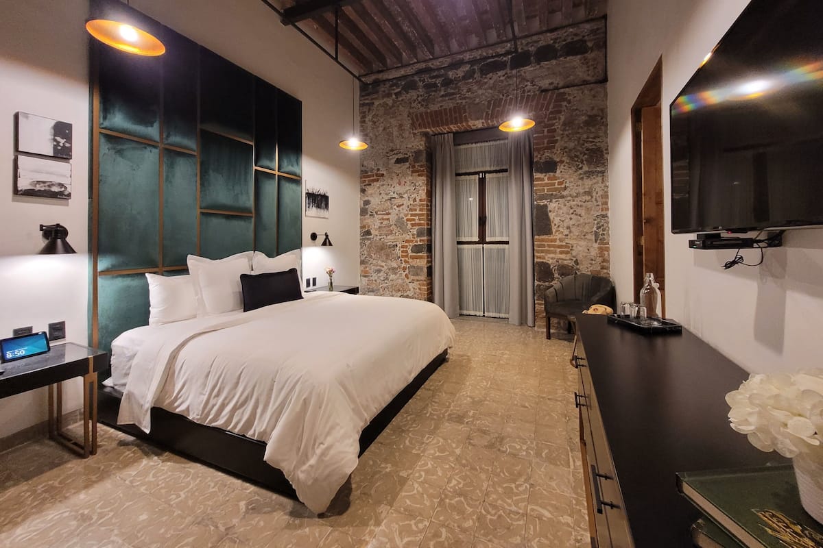 A modern bedroom with a large bed, a desk with a computer, and a TV mounted on the wall.