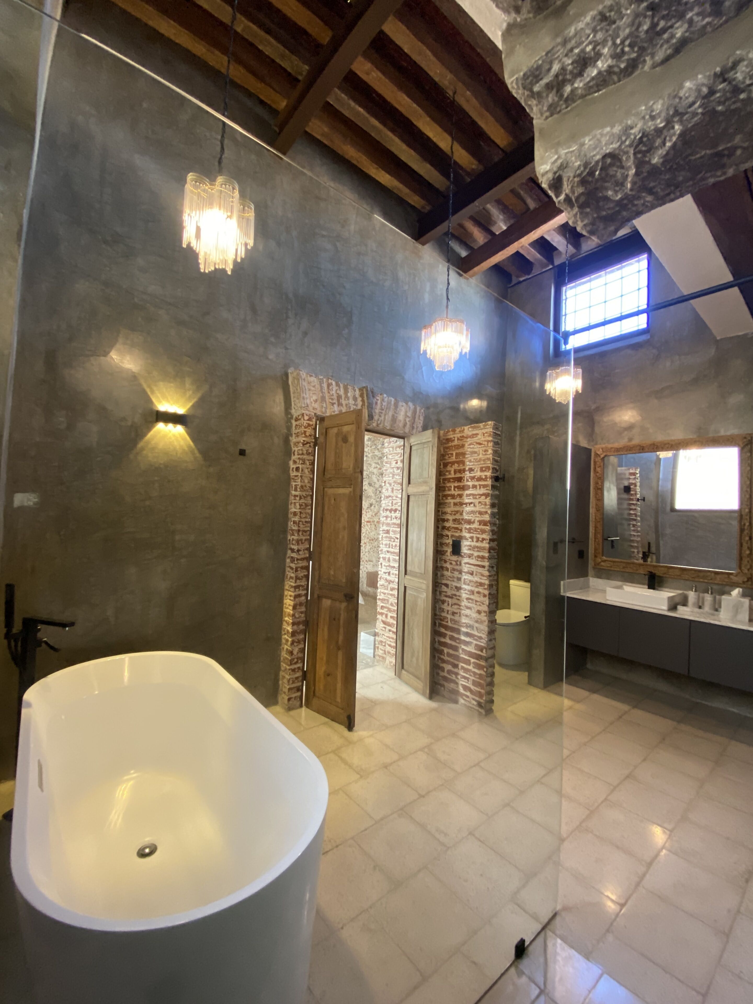 Een moderne badkamer met een vrijstaand bad, openliggende baksteenmuren en een grote spiegel.