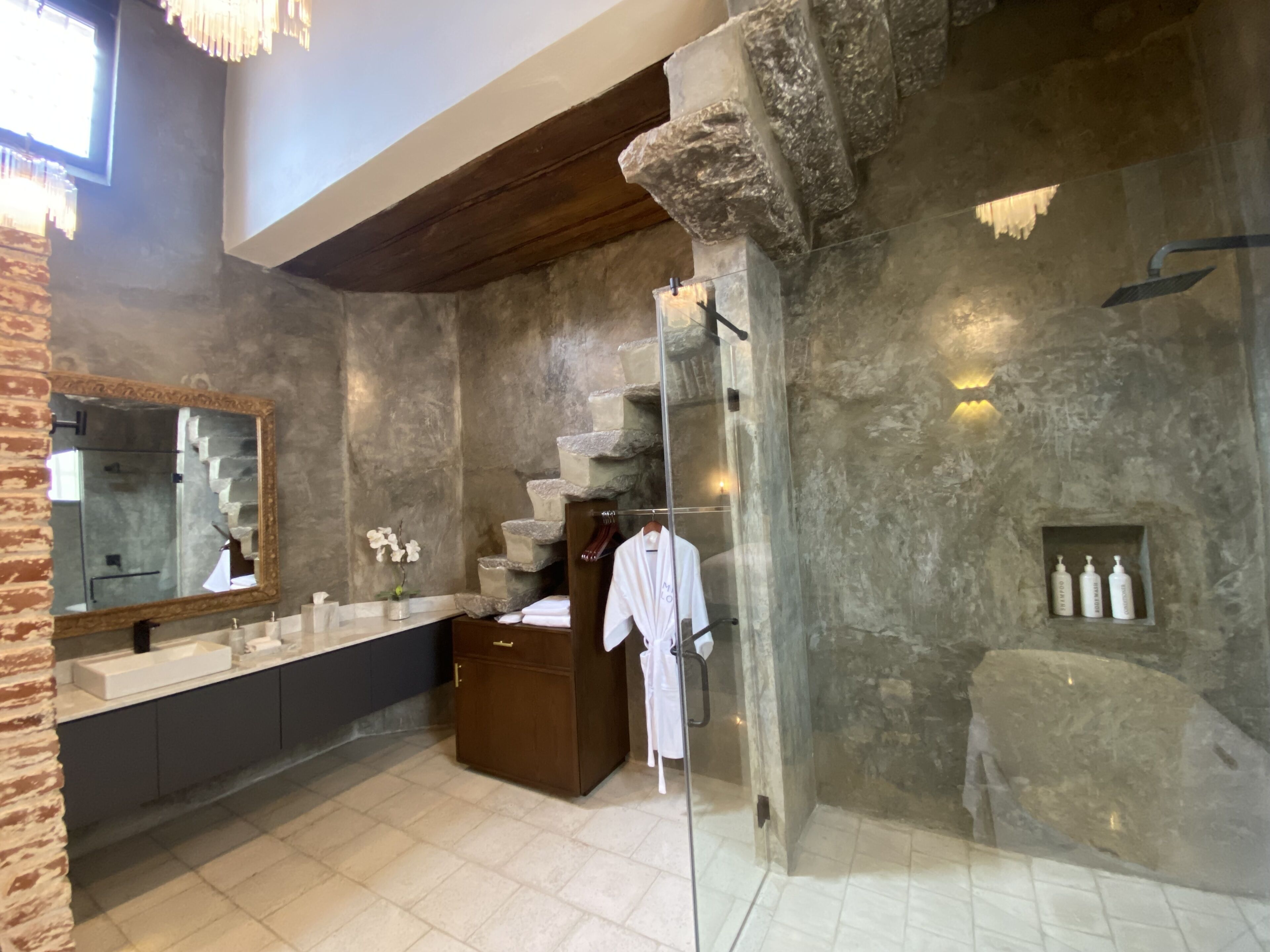 A modern bathroom with a stone wall, a large mirror, a wooden cabinet, and a glass shower enclosure.
