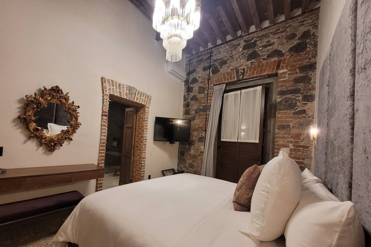 A bedroom with a large bed, a wooden dresser, a mirror, a TV, and a chandelier.