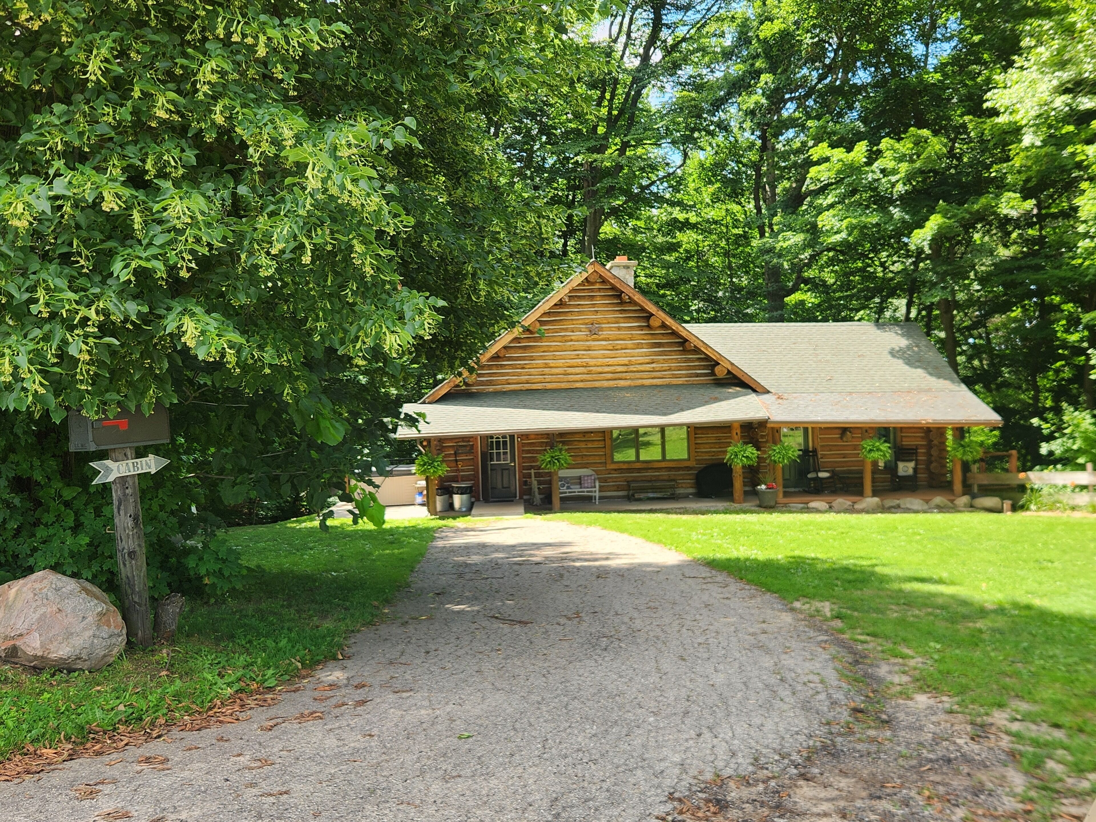 A log cabin with a porch, a gravel path leading to it, and a mailbox with a 'CABIN' sign.
