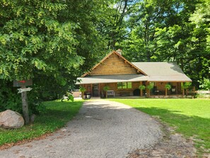 A log cabin with a porch, a gravel path leading to it, and a mailbox with a 'CABIN' sign. - Rare relaxation in your 3-bedroom Ranch cabin (Grand Rapids)