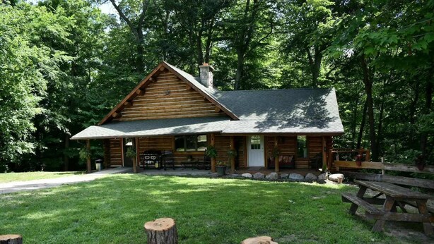 Una cabana de fusta amb un porxo, una barbacoa i una taula de picnic.