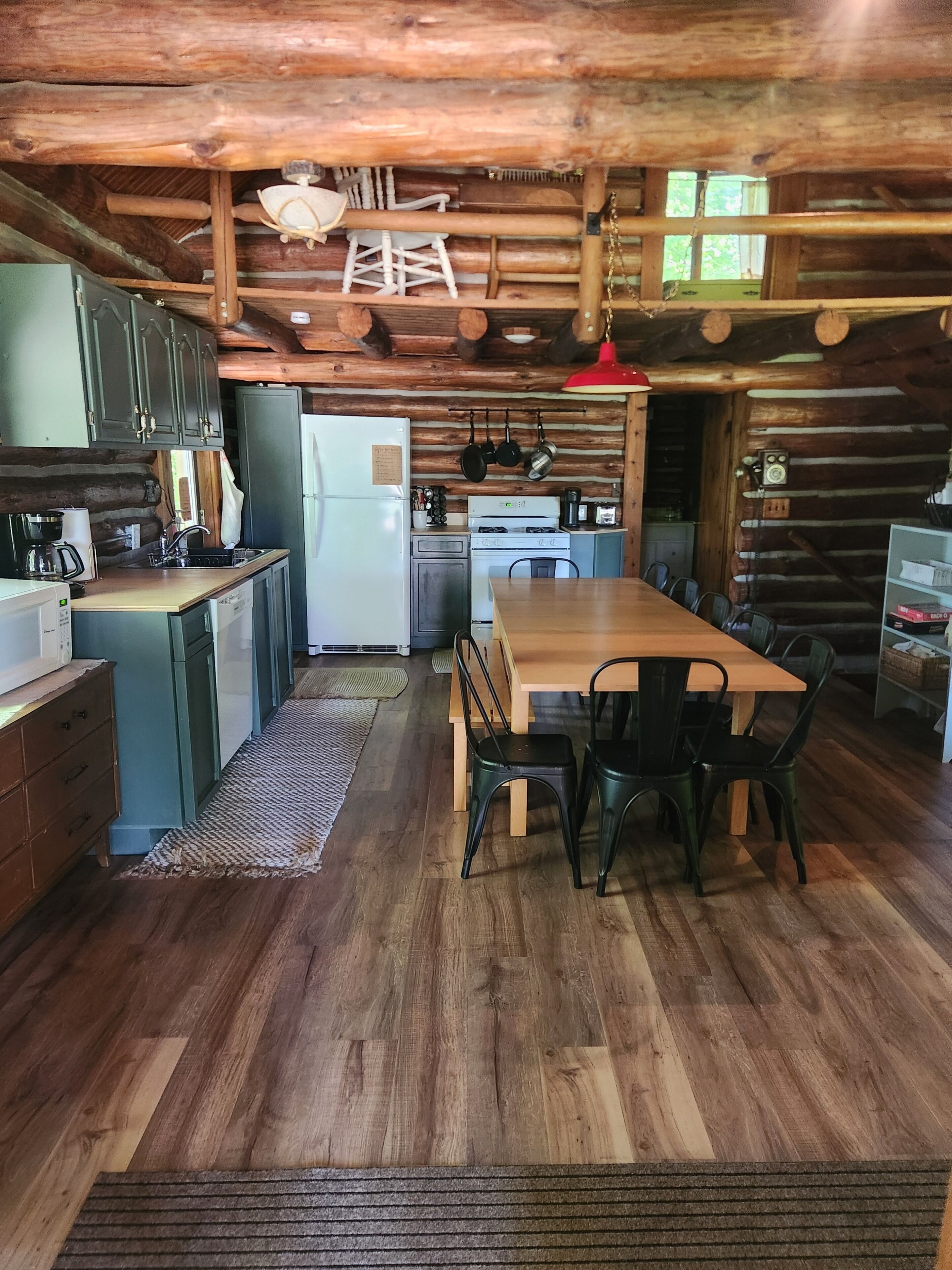 Ein rustikales Blockhaus-Interieur mit einem Holztisch, Stühlen, einer Küchenzeile inklusive Kühlschrank, Herd und hängenden Töpfen.