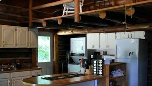 Interior rústic d'una cabana amb zona de menjador de fusta, tamborets, cuina amb armaris blancs i una illa gran.