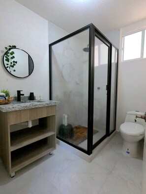 Une salle de bain avec un meuble-lavabo en bois, un miroir rond, une cabine de douche en verre et des toilettes.