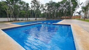 Une piscine rectangulaire à l’eau d’un bleu limpide, entourée d’une terrasse en béton et d’un petit muret.