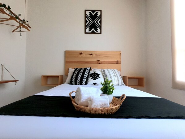 Un lit bien fait, avec une tête de lit en bois, deux tables de chevet et un élément décoratif fixé au mur.