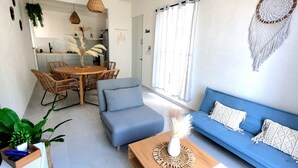 Un salon moderne avec un canapé bleu, une table basse en bois et un coin repas doté de meubles en osier.