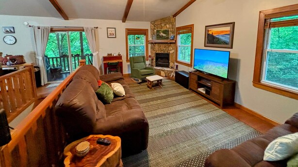 A cozy living room with a brown leather sofa, a television, a fireplace, and a stone wall.