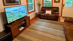 A living room with a television, a brown leather sofa, a patterned rug, and framed pictures on the wall.