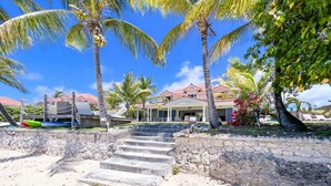 A beachfront property with a stone staircase leading to a covered area, palm trees, and a building with a red-tiled roof. - Beachfront villa private pool & stunning views (Saint-François)