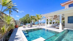 A clear blue pool with lounge chairs and a covered seating area, surrounded by palm trees and a view of the ocean. - Beachfront villa private pool & stunning views (Saint-François)