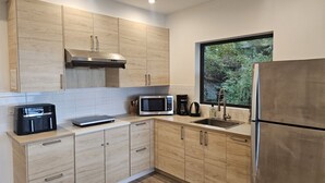 A modern kitchen with light wood cabinets, stainless steel appliances, and a window with a view of greenery. - J&J`s · Exquisite and brand new 1-bedroom ocean view suite (Bowen Island)