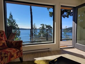 Een kamer met een groot raam met uitzicht op zee en bomen.