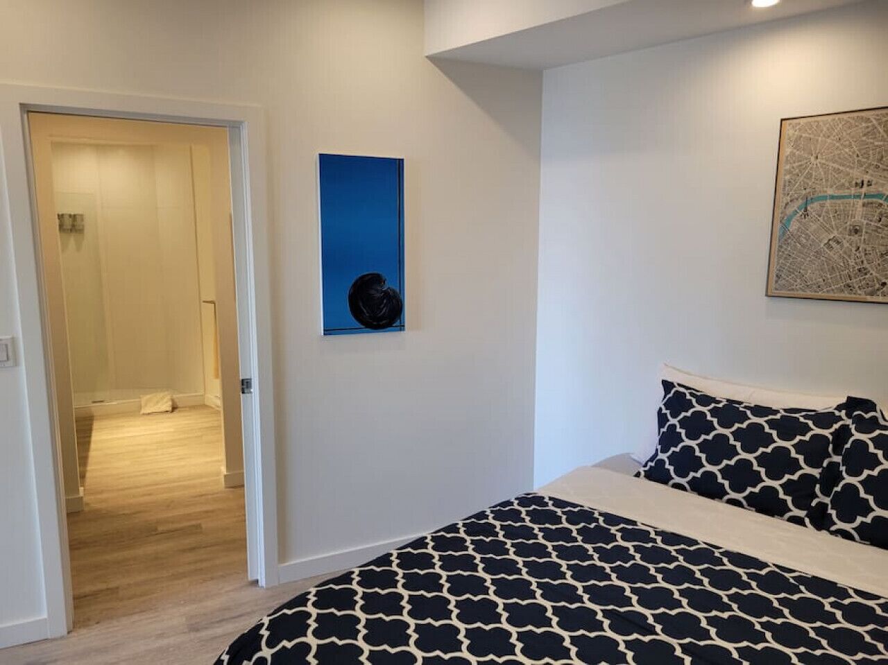 A bedroom with a bed, a door leading to another room, and a framed map on the wall.
