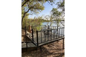 A wooden deck with a metal railing overlooking a body of water, surrounded by trees. - Lake Cabin with private dock and boat parking! (Cisco)