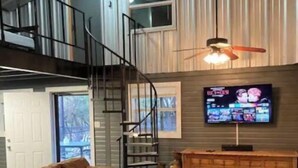 Una sala de estar amplia con un sofá seccional marrón grande, un mueble de entretenimiento de madera, un televisor de pantalla plana y una escalera que lleva a un nivel superior.