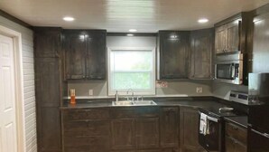 Una cocina con armarios de madera oscura, un lavamanos de acero inoxidable, un microondas y una estufa.