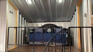 Una habitación con una cama, barandilla metálica y techo con luces.
