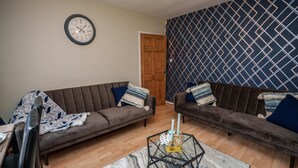 A living room with two sofas, a coffee table, a clock, and a patterned wall.