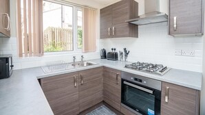 A modern kitchen with wooden cabinets, a gas stove, an oven, and a window with curtains.