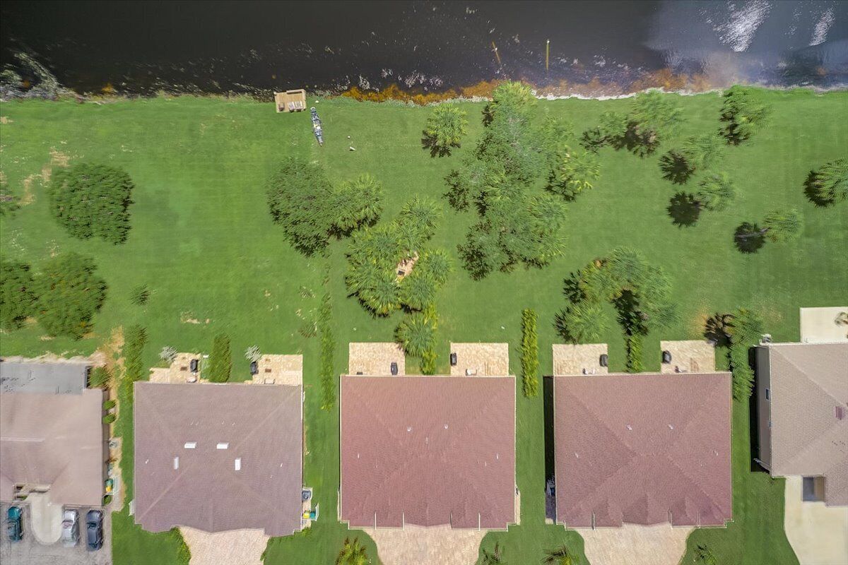 An aerial view of a residential area with multiple houses, a grassy field, and a body of water in the background.