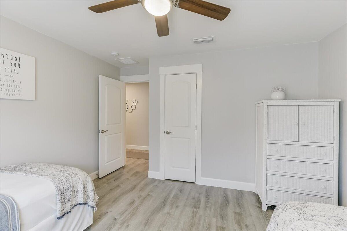 A bedroom with two beds, a white dresser, and a ceiling fan.