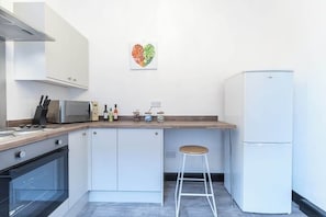 Eine kompakte Küche mit weißen Schränken, einer Mikrowelle, einem Kühlschrank und einer Holzausziehtafel.