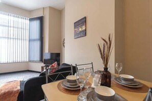 A dining area with a table set for four, a television, and a cityscape painting on the wall. - Ground floor 1 Bed Apt w/Garden & Street Parking (Kingston upon Hull)