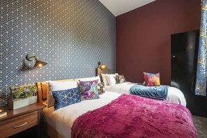 A hotel room with two beds, patterned wallpaper, decorative pillows, a nightstand, and a large window. - Ground floor 1 Bed Apt w/Garden & Street Parking (Kingston upon Hull)