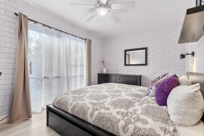 Een slaapkamer met een bed, een plafondventilator, een raam met gordijnen, een nachtkastje en een wandlamp.