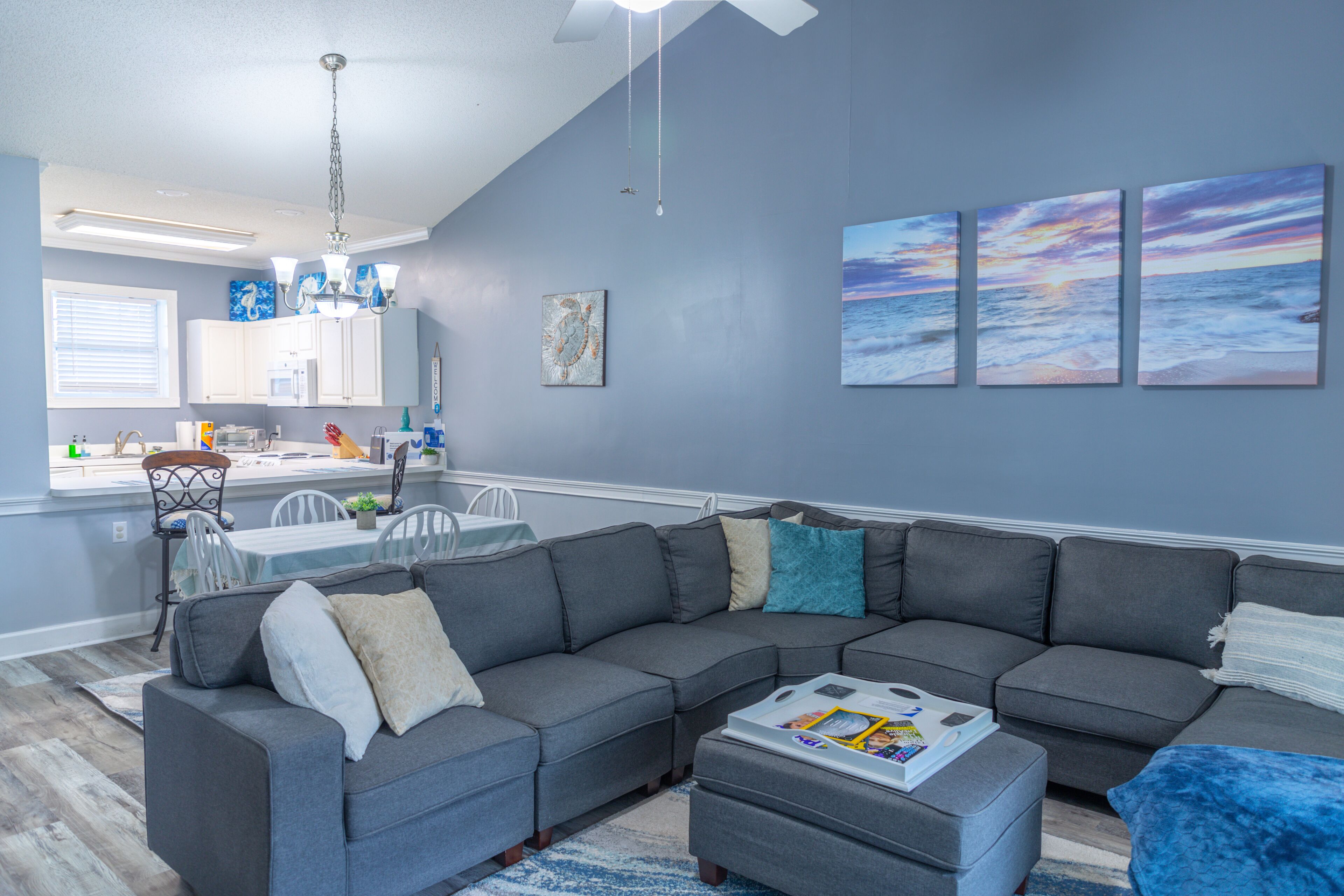 A modern living room with a sectional sofa, a dining area with a table and chairs, and a kitchen in the background.
