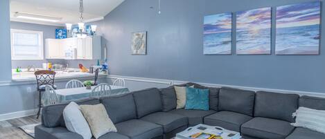 A modern living room with a sectional sofa, a dining area with a table and chairs, and a kitchen in the background.