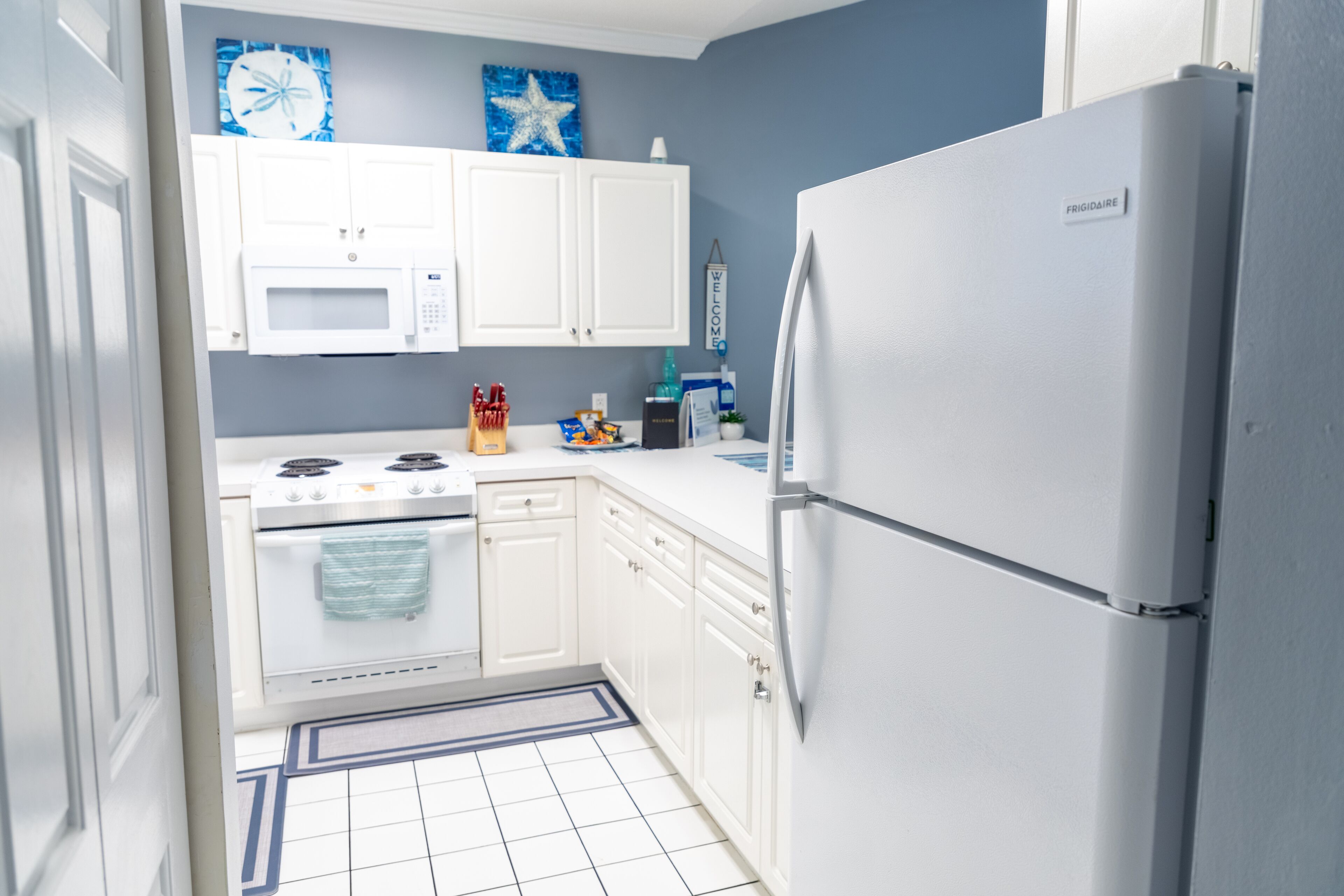 A compact kitchen with white cabinets, a stainless steel stove, a white refrigerator, and a microwave.