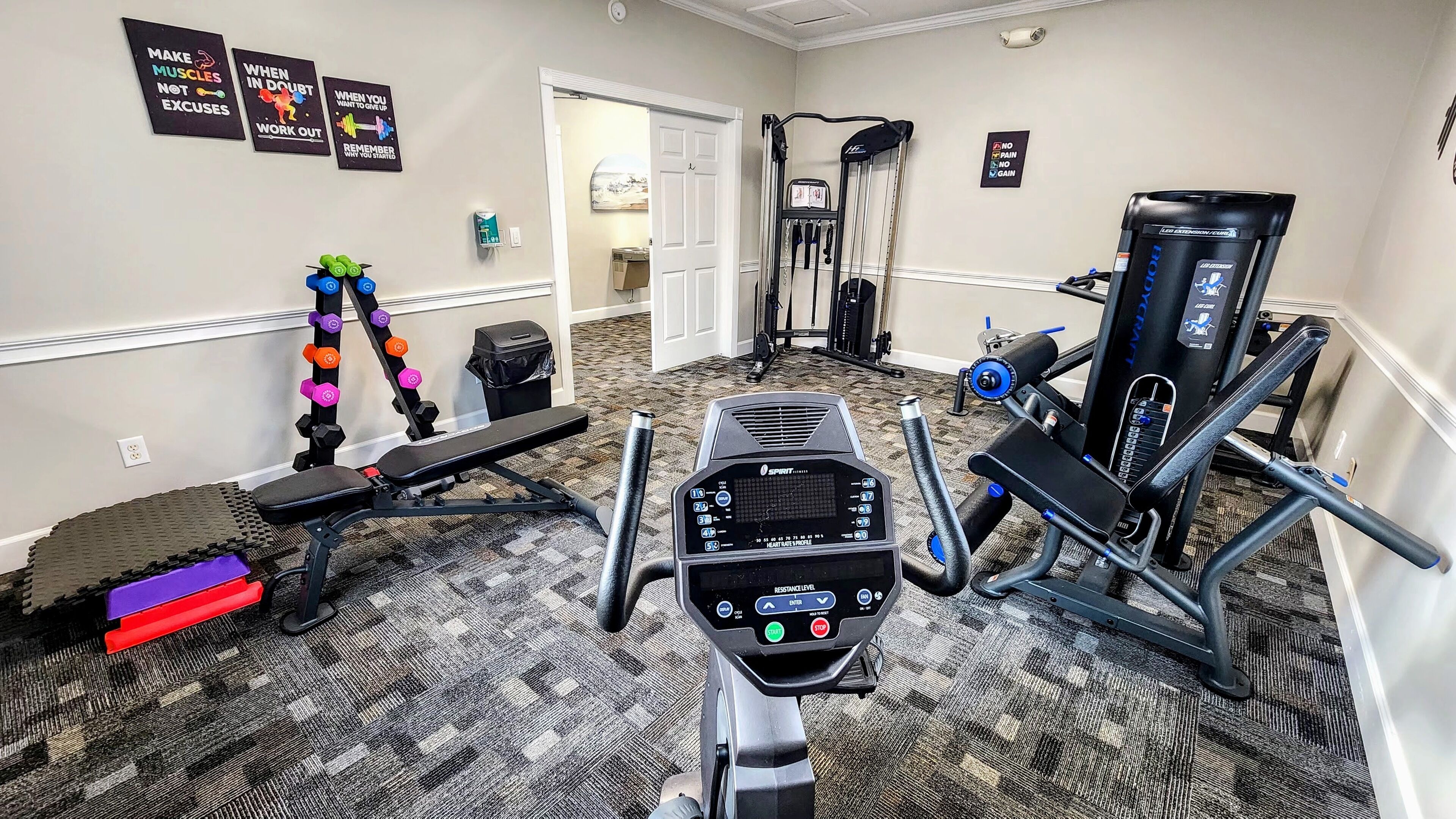Une salle de sport à domicile équipée d’un tapis de course, d’un banc de musculation, d’haltères et d’une machine à câbles.