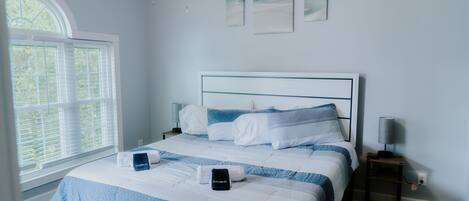A neatly made bed with a blue and white striped bedspread, a bedside table with a lamp, and a window with blinds.