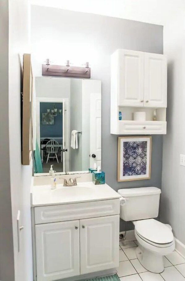 A bathroom with a white sink, mirror, and toilet. There is a cabinet above the toilet and a framed picture on the wall. - Water View! Serene Myrtle Beach Condo & Breathtaking View, King Suite, 3 Pools (Myrtle Beach)