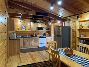 A wooden cabin interior with a kitchen, dining area, and a ceiling fan. - Viola River Lodge (Timberville)