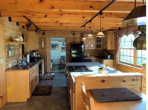 A wooden cabin kitchen with a central island, wooden cabinets, and pendant lighting. - Viola River Lodge (Timberville)