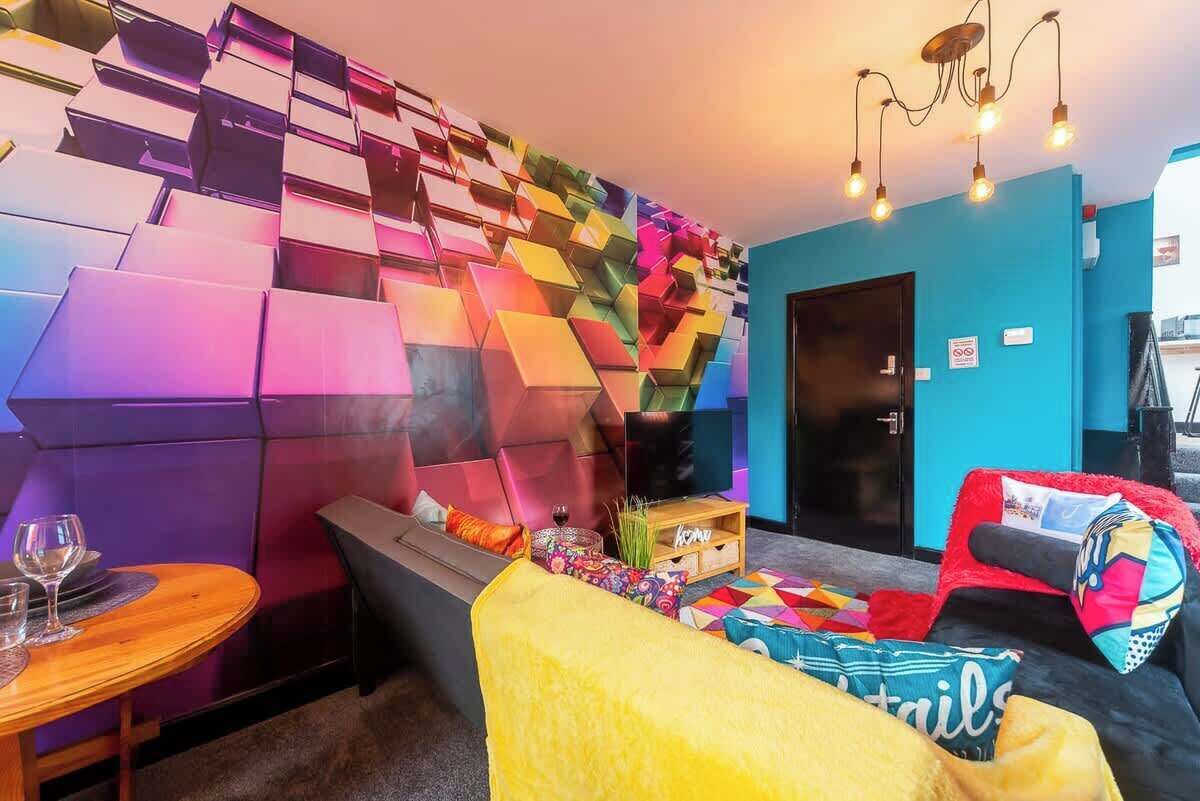 A modern interior with a colorful geometric wall, a sofa, a small table with a glass, and a television.