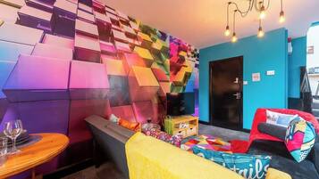 A modern interior with a colorful geometric wall, a sofa, a small table with a glass, and a television.
