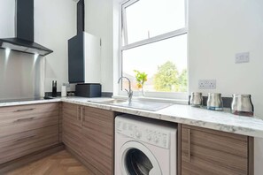 A modern kitchen with a built-in washer, a stainless steel range hood, and a window with a view of greenery.