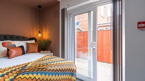 Ein Schlafzimmer mit einem Bett, Kissen, einer Nachttischlampe und einer Schiebetür zu einem Innenhof.