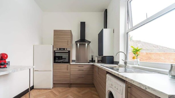 Eine moderne Küche mit Einbauofen, Edelstahl-Dunstabzugshaube, Waschmaschine und einem Fenster mit Blick ins Freie.