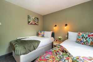 A hotel room with two beds, a painting on the wall, and two wall-mounted lamps.