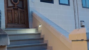 Eine Treppe führt zu einer Holztür mit Glasfenster, einem kleinen Fenster und einem Schild mit der Nummer 76.